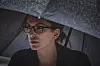 Young woman holding umbrella, walking outdoors and struggling with a wind and rain on a cold autumn day.
