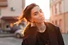 Portrait of a young cute attractive woman with a stylish hairstyle with beautiful eyes with sexy lips in fashionable black clothes on a background of bright orange spring sunset. Elegant girl relaxes.
