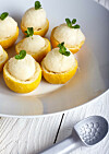 Lemon icecream served in half of lemon in white plate on white background. Ice creame scoop near it.