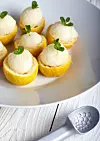 Lemon icecream served in half of lemon in white plate on white background. Ice creame scoop near it.