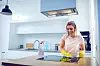 Worthy cheerful caucasian blond housewife with rubber gloves on hands cleaning stove. Kitchen interior.