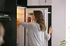 Happy woman opening the fridge and taking food from the upper shelf