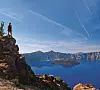 Girl looks out over the expanse of the deep blues of Crater Lake standing on a precarious rock outcrop