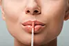 close up on lip gloss near shiny lips of woman isolated on grey