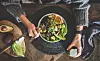 Healthy dinner, lunch setting. Flat-lay of vegan superbowl or Buddha bowl with hummus, vegetable, salad, beans, couscous and avocado, green smoothie and woman's hands over wooden table, top view