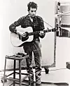 Bob Dylan (b. 1941) playing guitar and harmonica into microphone. 1965.