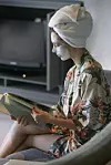 Young woman sitting at home with face beauty mask while reading a book. Cozy time at home. Self time and home spa concept. Coronavirus outbreak and self-quarantining concept.