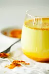 Healthy ayurvedic drink golden almond milk or pumpkin turmeric latte with curcuma powder on white background close-up. Trendy Asian natural detox morning beverage with spices for vegans. Vertical orientation