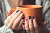 Woman with beautiful manicure holding a orange cup of cocoa