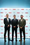 Troje muškaraca u odijelima pozira ispred zida s logotipima HBO-a.