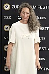 Olivia Colman u bijeloj haljini pozira pred logotipima na Zurich Film Festivalu.