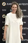 Olivia Colman u bijeloj haljini pozira pred logotipima na Zurich Film Festivalu.