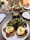 Tanjur s dva jaja Benedict, umakom, slaninom i salatom na stolu za brunch.