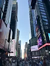 Gužva pješaka na Times Squareu između nebodera s velikim digitalnim reklamnim ekranima.
