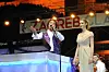 Tonči Huljić u ljubičastom sakou pjeva uz mikrofon, a Hana Huljić u dugoj bež haljini stoji kraj njega.