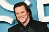 Jim Carrey u crnom smokingu nasmiješen pozira pred pozadinom nagrada César u Parizu.