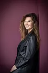 Martina Validžić nasmiješena pozira u crnoj kožnoj jakni ispred tamnoljubičaste pozadine.