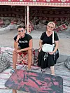 Dvije žene u ležernoj odjeći sjede na jastucima među šarenim tepisima i tkaninama.