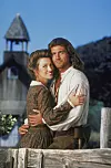 Jane Seymour i Joe Lando u povijesnoj odjeći zagrljeni ispred drvene crkve.