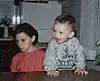 Djevojčica u ružičastoj majici i dječak u majici Disney Baby sjede za stolom.