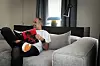 Muškarac u bijeloj majici i crnim hlačama čita crveni časopis na sivom kauču.