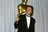 Michael Douglas u crnom smokingu drži Oscar za film „Wall Street” ispred srebrne zavjese.