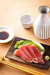Narezani sashimi od tune s wasabijem na tamnom drvenom pladnju, uz štapiće i umak od soje.