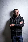 Juraj Šebalj u crnoj jakni i trapericama prekriženih ruku pozira uz teksturirani zid.