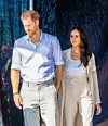 Princ Harry u svijetloj košulji i Meghan Markle u bež odijelu hodaju jedno uz drugo.