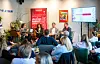 Panelisti sjede ispred crvenog promotivnog panoa, dok ih publika prati u dvorani