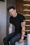 Marko Braić u crnoj majici i trapericama sjedi na drvenom stubištu u svom domu.
