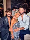 Žena u srebrnoj haljini sa šljokicama pozira između dvojice muškaraca u elegantnoj odjeći.