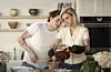 Brooklyn Beckham u bijeloj majici i Nicola Peltz u svijetloj odjeći kuhaju zajedno u kuhinji.