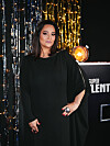 Žena u dugoj crnoj haljini pozira uz svjetlucavu pozadinu emisije Supertalent.