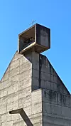 Visoka betonska građevina s križem na vrhu pod vedrim plavim nebom.