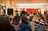 Publika gleda glazbeni nastup izvođača na pozornici u trgovačkom centru.