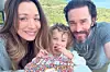 Kaley Cuoco i Tom Pelphrey poziraju s djetetom uz šarenu tortu na otvorenom.