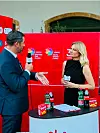 Žena u crnoj haljini razgovara s muškarcem u odijelu uz stol s promotivnim napitcima.