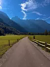 Asfaltirana cesta kroz zelenu dolinu vodi prema visokim planinama pod plavim nebom.