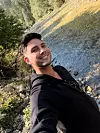 Mladić u crnoj majici snima selfie na kamenitoj planinskoj padini.