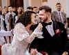 Mladenka u čipkastoj haljini šapće mladoženji u crnom odijelu tijekom vjenčanja.