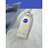 Bočica NIVEA Q10 mlijeka za tijelo na bijeloj tkanini uz plavi pleteni tekstil.