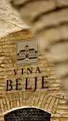 Kameni zid podruma s natpisom Vina Belje, uokvirenom ilustracijom i policom boca.