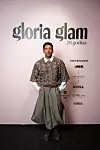 Muškarac u pletenom puloveru i širokim hlačama pozira na događanju Glorije Glam.