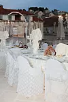 Svečani bijeli stol s čipkastim stolnjakom i ukrasima na otvorenom u Hvaru, uz kamene kuće i crvene krovove.