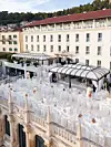 Raskošno uređena krovna terasa s bijelim stolovima ispred velike povijesne zgrade.