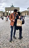 Dvoje ljudi u zagrljaju ispred Brandenburških vrata; osoba u kožnoj jakni nosi uzorčastu papirnatu vrećicu.