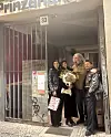 Skupina ljudi u tamnoj odjeći pozira s buketom cvijeća na ulazu u zgradu.