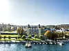 Povijesni hotel uz jezero Wörthersee s vrtovima, molovima i čamcima, u podnožju zelenih brežuljaka.