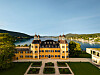 Falkensteiner Schlosshotel Velden uz jezero, s vrtovima, šumovitim brežuljcima i planinama u pozadini.